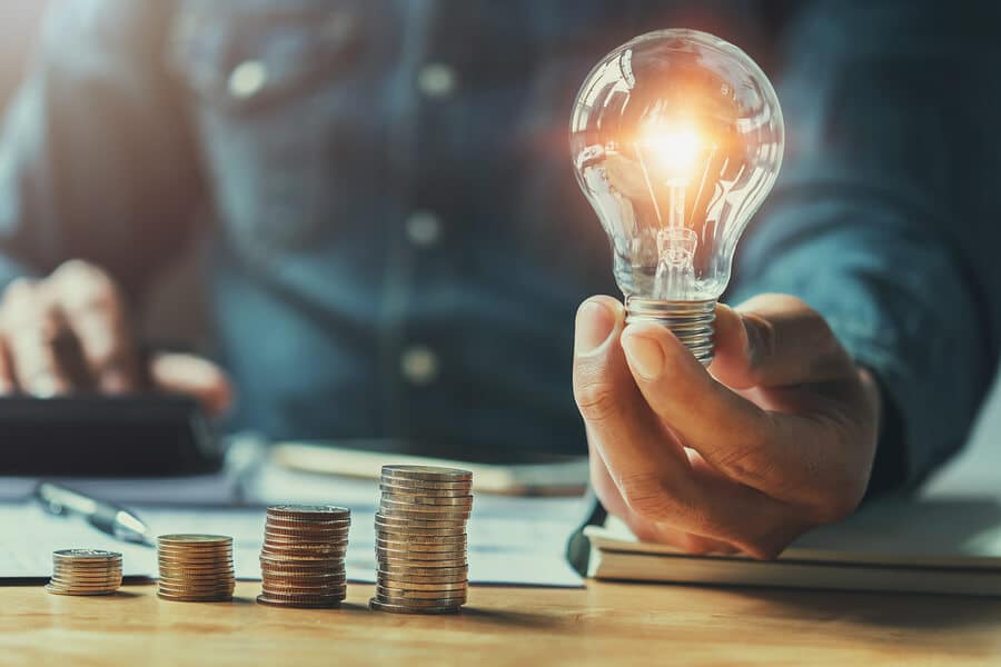 A hand holding a light bulb and coins on a desk illustrating innovation in the VoIP industry.