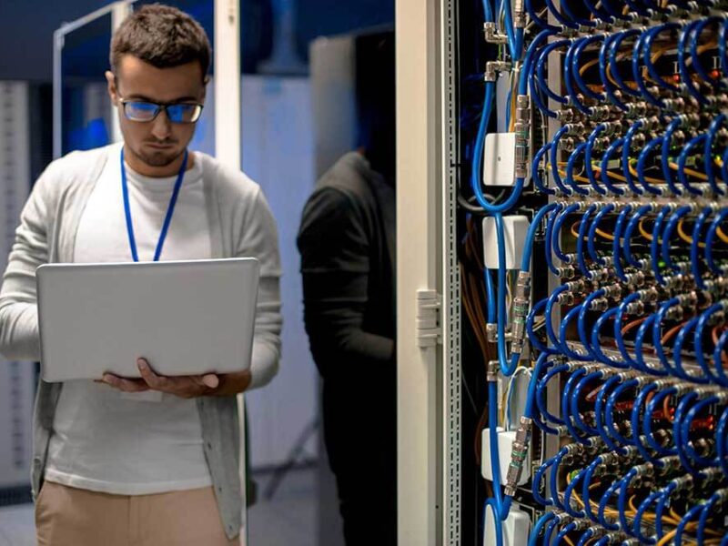 A man providing Managed IT Services, looks at a laptop in a server room.