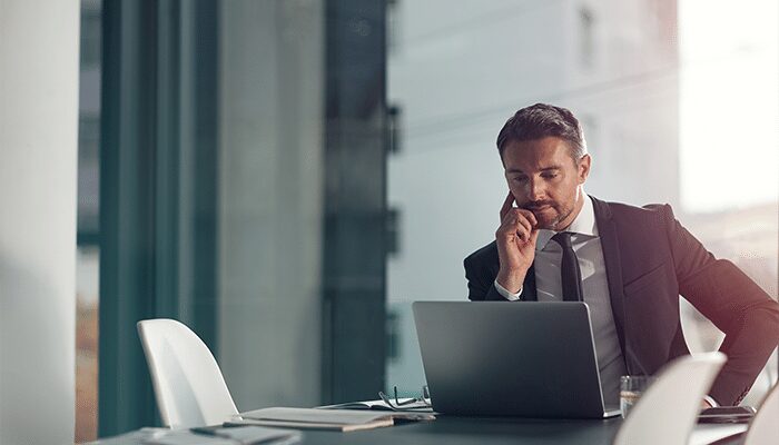 A man in a suit is talking on the phone while sitting in front of a laptop.