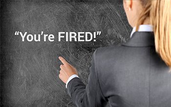 A business woman pointing at a chalkboard that says you're fired.