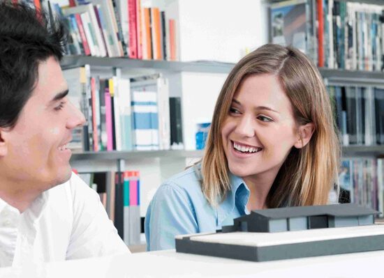 A man and woman sitting in a library looking at a computer.