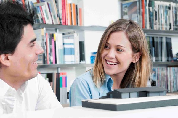 A man and woman sitting in a library looking at a computer.