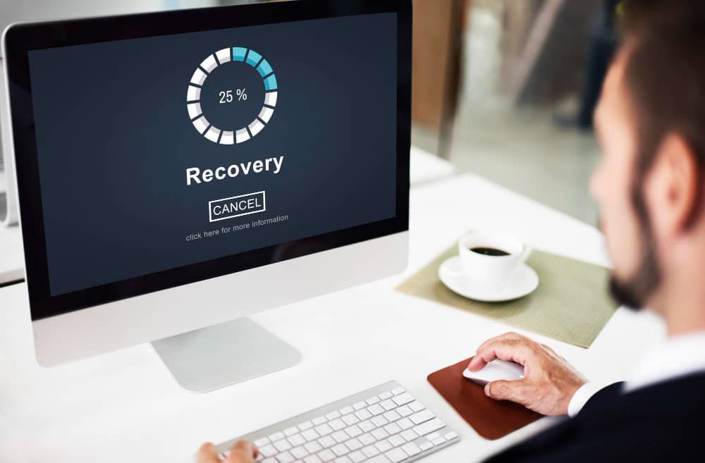 A man sitting at a desk with a computer screen showing Worcester's recovery percentage through Managed IT Services.