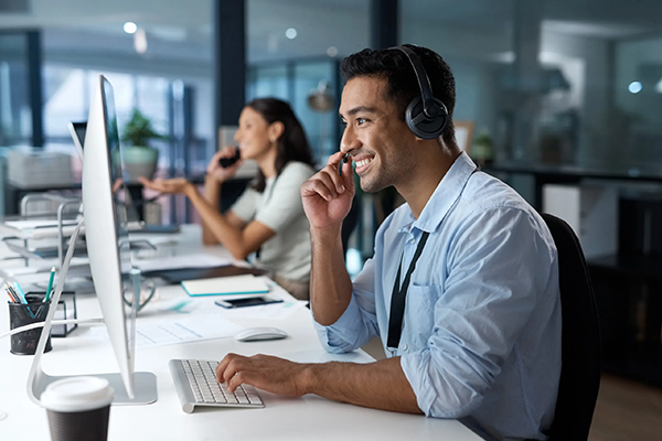 A man wearing a headset and a woman sitting at a desk managing outsourced IT.