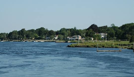 A calm, wide river with houses and green trees along the far bank, under a clear blue sky in Barrington, where even managed IT services feel serene and seamless.