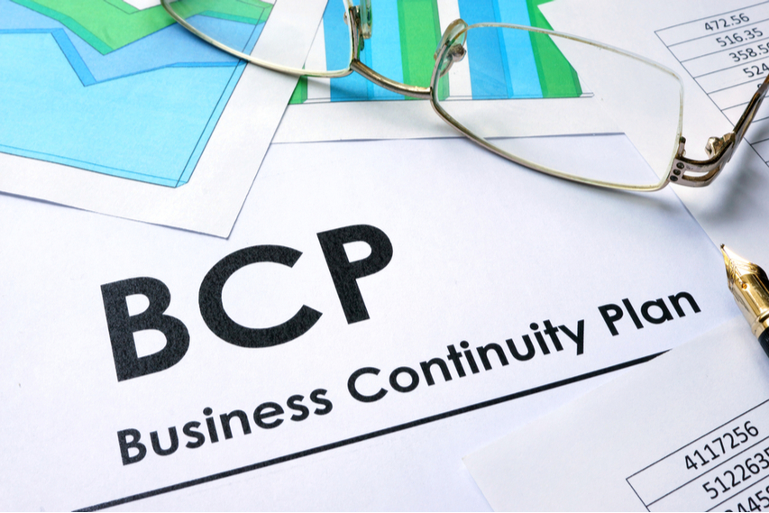 Close-up of a document titled "Business Continuity Plan" with glasses resting on top, next to charts and a pen.