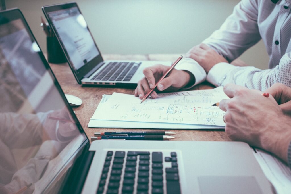 Two people sit at a table with laptops open, reviewing printed documents, making notes with pencils, and discussing IRS Publication 4557 safeguarding taxpayer data during their collaborative work session.