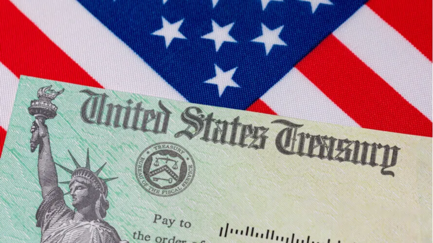 A United States Treasury check is shown in front of part of an American flag with white stars on a blue background and red and white stripes, symbolizing the importance of IRS Publication 4557 safeguarding taxpayer data.